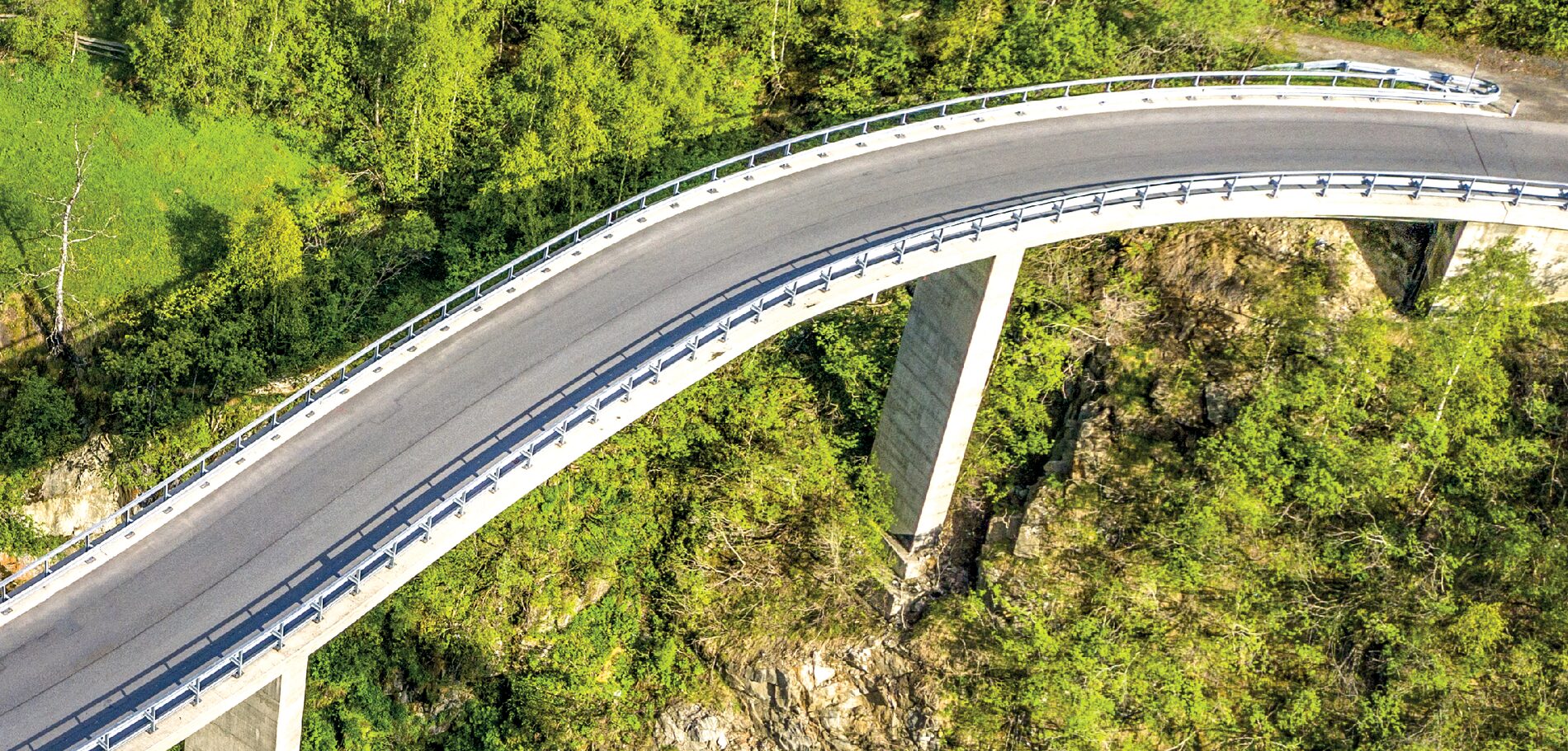 Luftbild einer geschwungenen Straßenbrücke auf Betonpfeilern über einer bewaldeten Schlucht