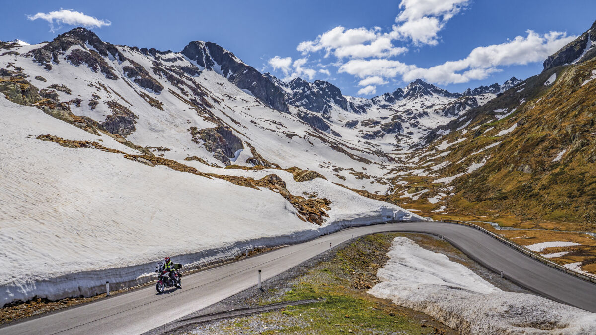 Motorrad auf einer Straße zwischen meterhohen Schneewänden, dahinter ein Talkessel mit Firnfeldern
